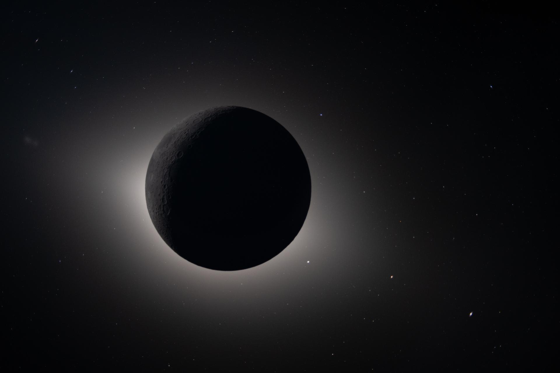 the moon blocking the Sun glowing back lit. Stars and planet are visible as bright dots around the Moon