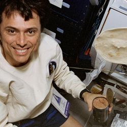 astronaut is smiling at the camera holding a bean can with a tortilla floating around
