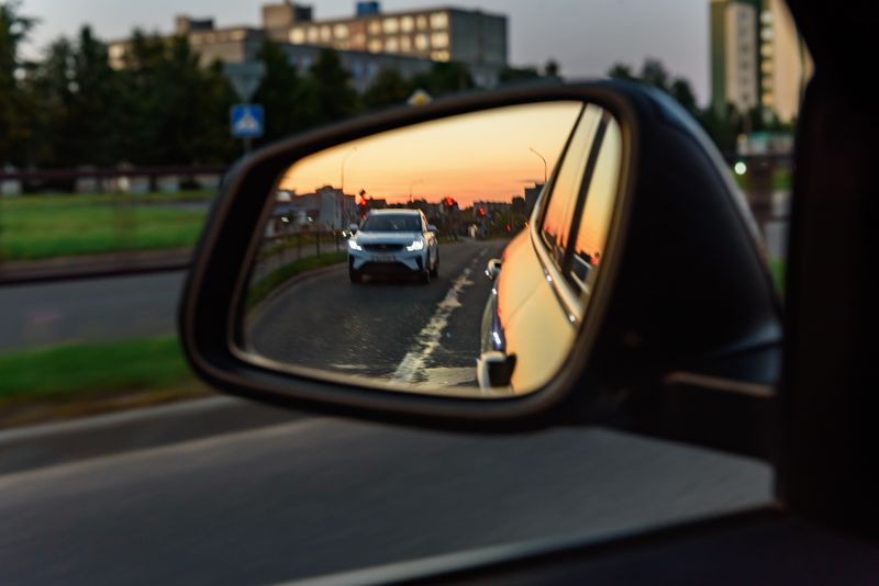 car wing mirror reflecting the car behind, at sunset