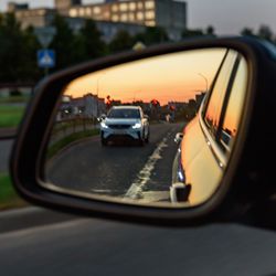 car wing mirror reflecting the car behind, at sunset