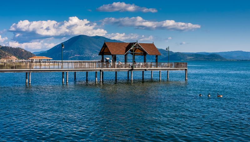 a pier jutting out onto Clear Lake in California on a sunny day, mountains are visible in the background