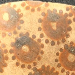 A pottery shard with around six crudely painted cirlces with dots around them to look like flowers 