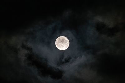A photo taken of the full moon in a cloudy night sky. The moon itself is framed in the picture's center with darker and lighter clouds surrounding it.