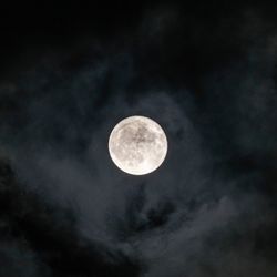 A photo taken of the full moon in a cloudy night sky. The moon itself is framed in the picture's center with darker and lighter clouds surrounding it.
