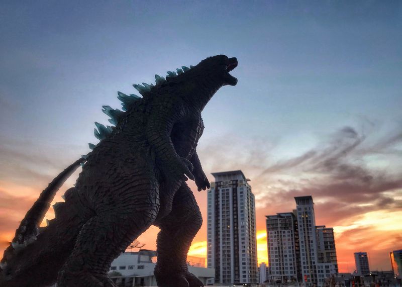 A silhouette of a godzilla, giant reptile monster infront of a cityscape.