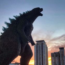 A silhouette of a godzilla, giant reptile monster infront of a cityscape.
