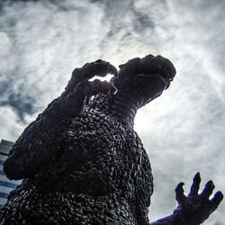 godzilla statue photographed from below with a cloudy sky and a high-rise building in the background