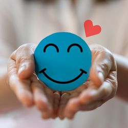 hands holding out a blue paper circle with a smiley face on it and red heart next to it
