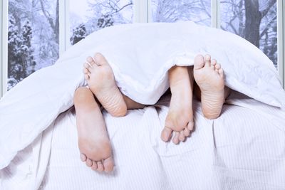 shot from the end of a bed with two people's feet sticking out under the duvet; there's a window behind the bed showing a wintry snowy scene