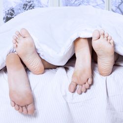 shot from the end of a bed with two people's feet sticking out under the duvet; there's a window behind the bed showing a wintry snowy scene