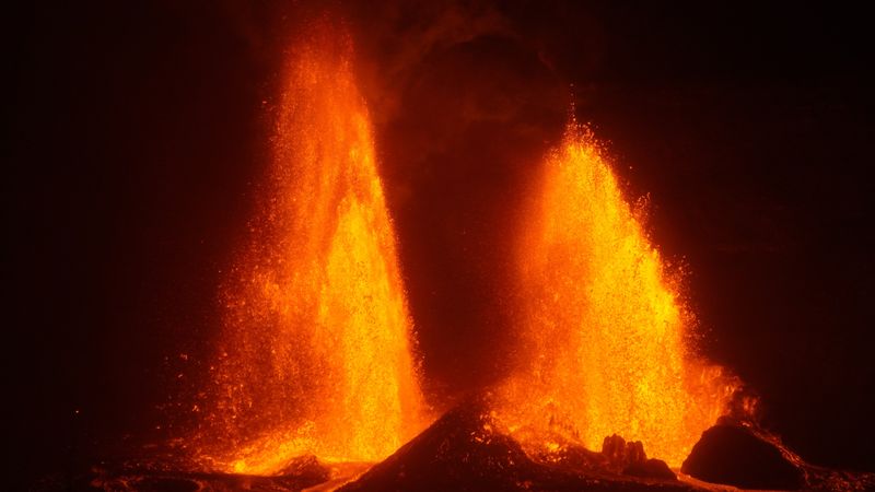 Two bright orange lava fountains erupting against a dark sky