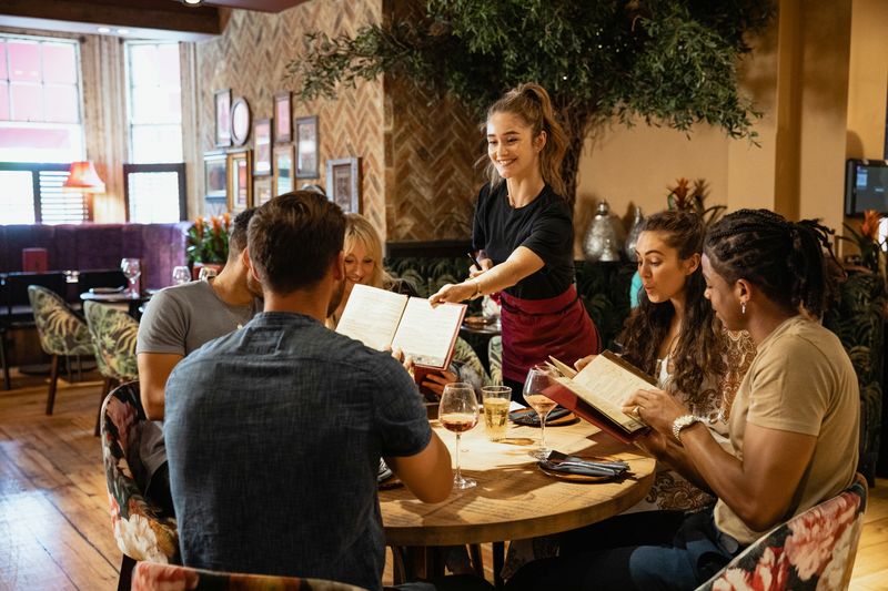 A group of friends looking at menus together in a restaurant, which have been given to them by a waitress. 