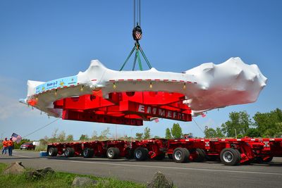 a massive ring with red metal support structure in the middle is being lifted on the back of a flat lorry