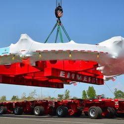 a massive ring with red metal support structure in the middle is being lifted on the back of a flat lorry