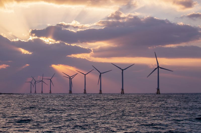 An offshore wind turbine farm in the sea with a sunset ehind