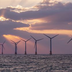 An offshore wind turbine farm in the sea with a sunset ehind