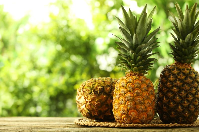 Fresh ripe pineapples on wooden table against blurred background