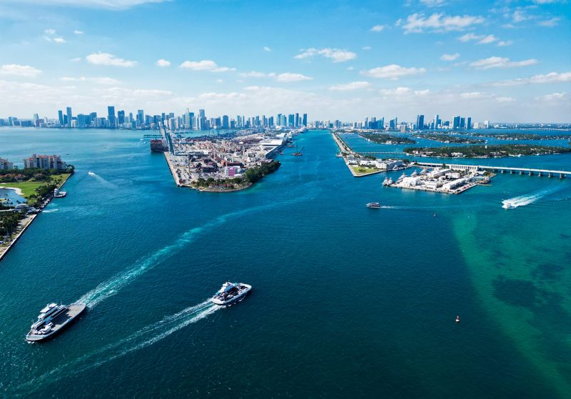 An aerial view of a the port of Miami with shipping boats and large buildings in the background.