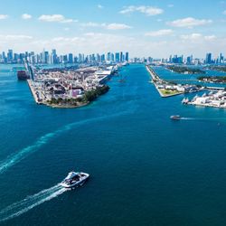 An aerial view of a the port of Miami with shipping boats and large buildings in the background.