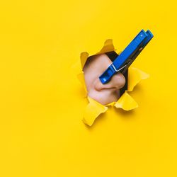 nose with blue clothespin on it breaking through hole in yellow paper