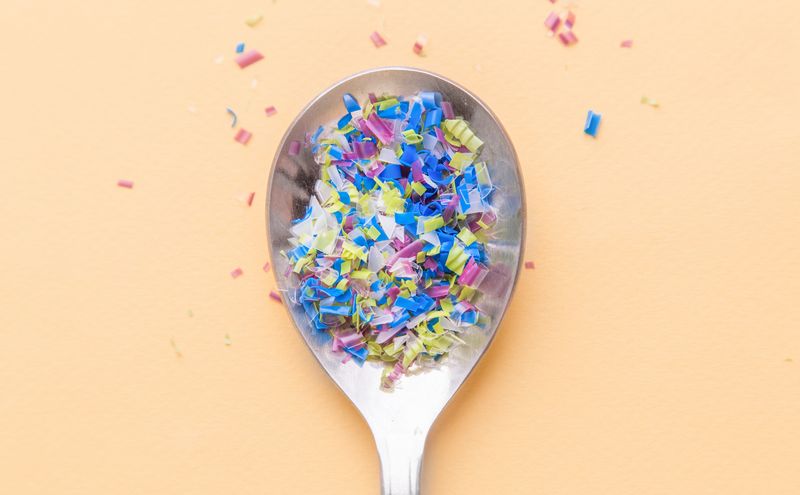 top-down view of a metal spoon filled with small, multicolored pieces of plastic