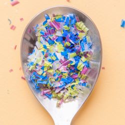 top-down view of a metal spoon filled with small, multicolored pieces of plastic
