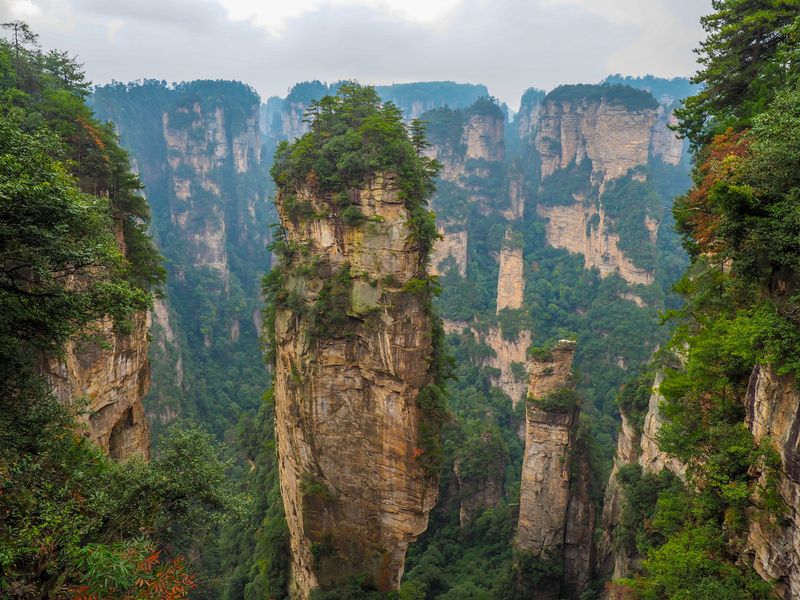 Huge soaring sandstone pillars covered in greenery soar into the sky as clouds float above ther tops