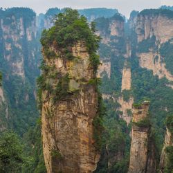Huge soaring sandstone pillars covered in greenery soar into the sky as clouds float above ther tops