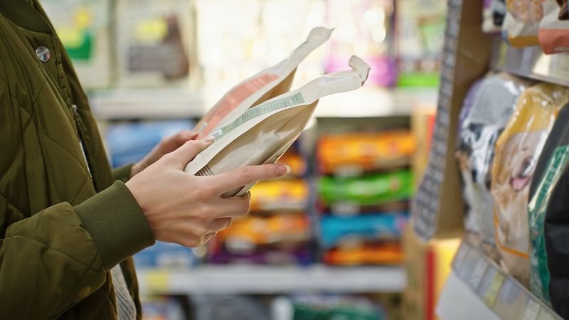 A photo showing a woman holding two bags of coffee. The photo has been cropped so that it is focusing on her hands only. She is standing on profile facing a shelf of coffee that is just visible to the right of the image. 