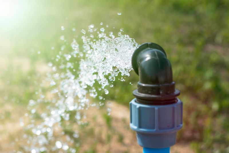 water spurting out of a black and blue PVC pipe onto some grass