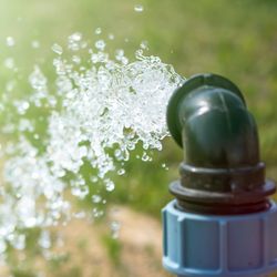 water spurting out of a black and blue PVC pipe onto some grass