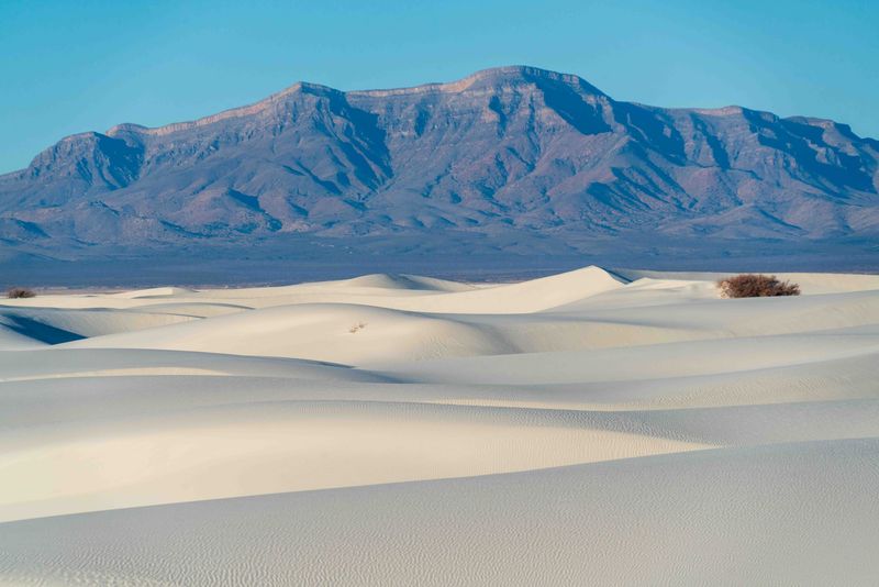 in the foreground, there are white sand dunes; mountains overlook them in the background