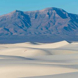 in the foreground, there are white sand dunes; mountains overlook them in the background