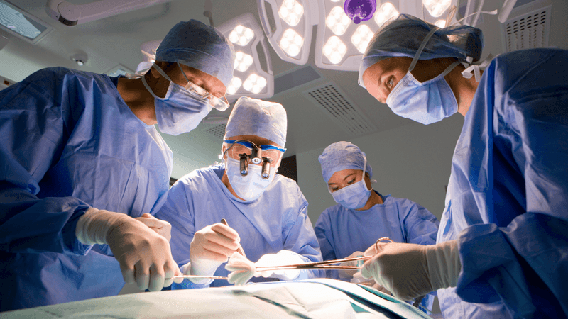 a groupof doctors and nurses stand around a patient in the sterile field of an operating theater