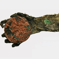 A mummified green hand, holding a copper coin.