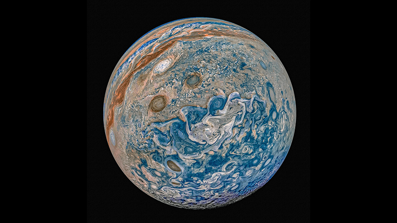 A beautiful prcoessed image of Jupiter showing it's swirling storms and gasses in reds, blues and greens using JUNO data.