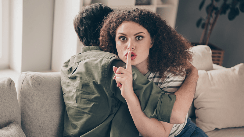 A woman hugging a man and making a "shush" gesture.