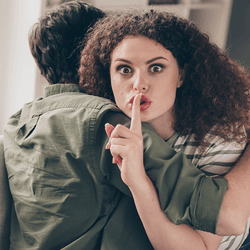 A woman hugging a man and making a "shush" gesture.